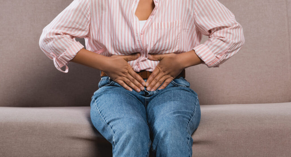 partial view of african american woman suffering from abdominal pain while sitting on sofa in living